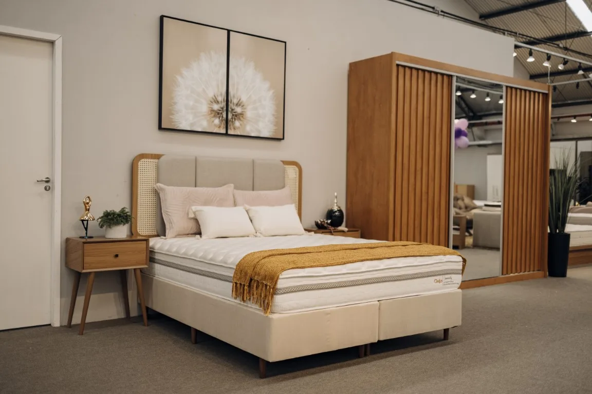 Cama box de casal macia Immensity montada em um quarto sofisticado, com roupeiro ripado e guarda-roupa espelhado ao fundo.