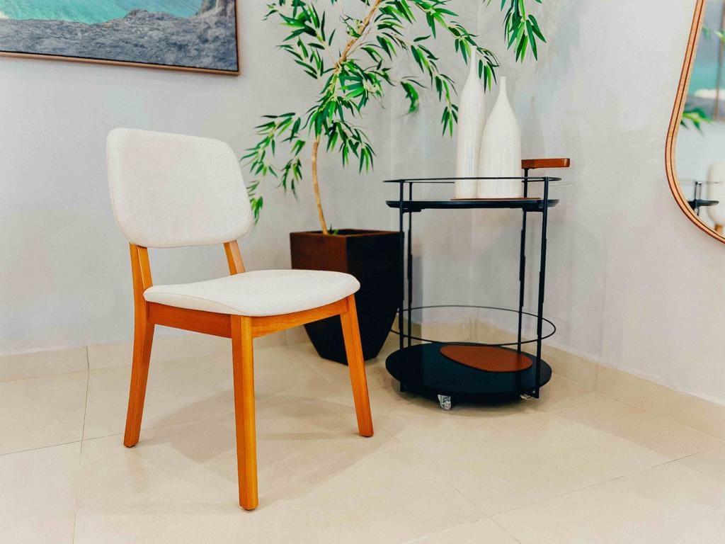 Cadeira Classic Sala de Jantar Decorada - Design Atemporal Cadeira Classic estofada posicionada em ângulo em uma sala decorada, ao lado de um vaso marrom e carrinho bar preto.