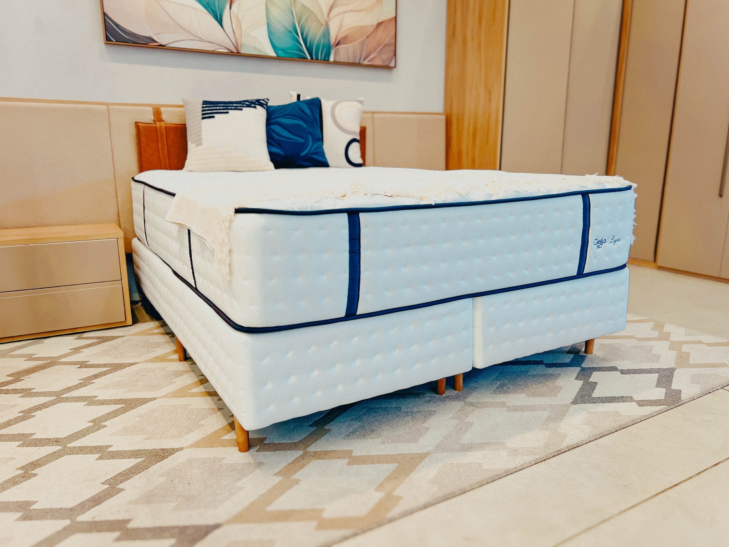 Conjunto Box Ciello Lyon Quarto de Luxo Cama box branca com detalhes azuis e tecnologia Sense Ice em um quarto moderno com tapete geométrico.