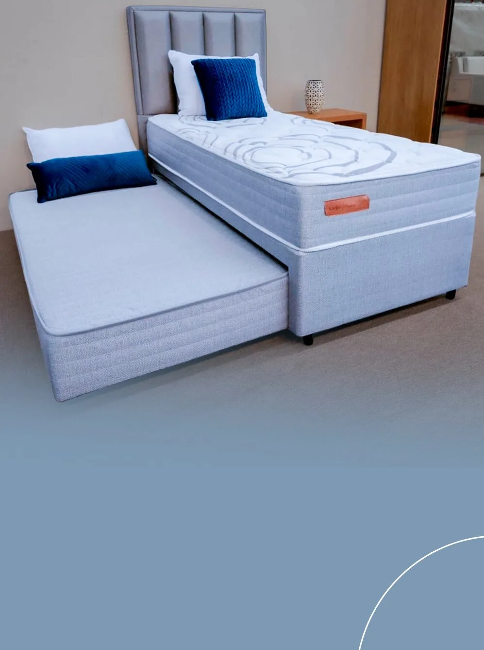 Cama box de solteiro em tecido cinza com a cama auxiliar puxada na parte inferior e cabeceira alta estofada com gomos verticais.