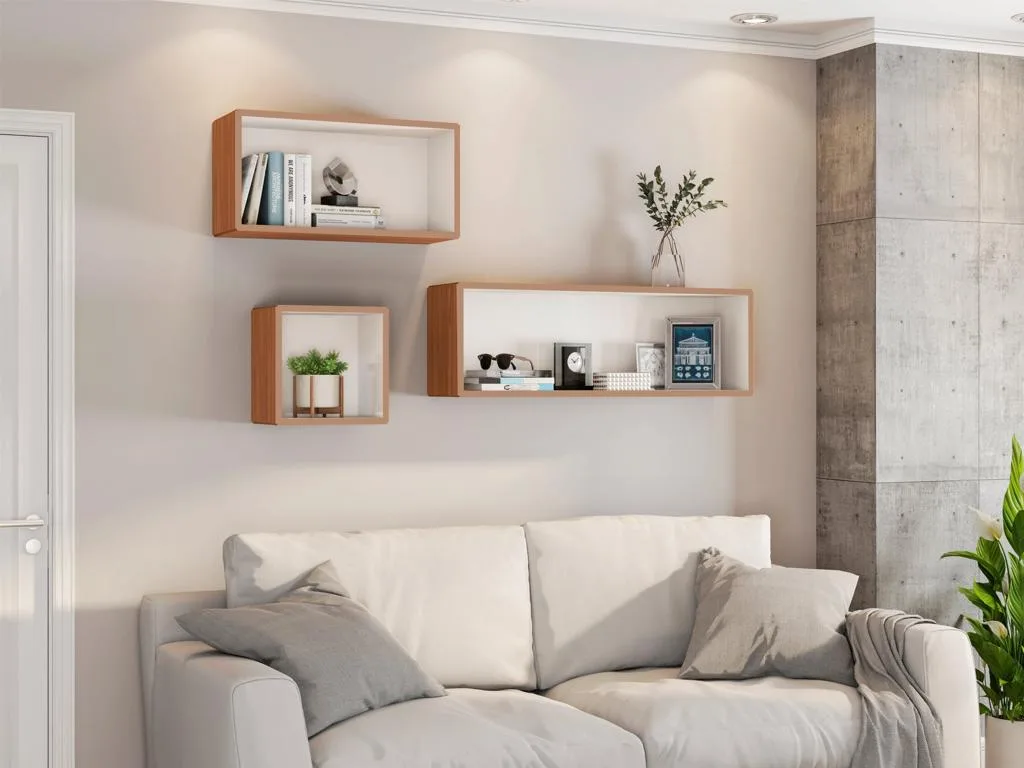 Decoração de sala de estar moderna com um sofá claro e almofadas cinzentas. Na parede bege superior, estão instalados três nichos de MDF amadeirados modulares da linha TB150 em posições diferentes, decorados com livros, quadros e plantas.